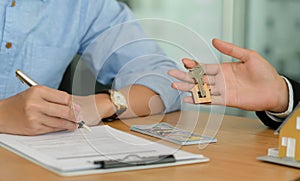 Close-up shot of Homebuyers signing home contracts and house brokers holding house key photo