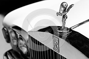 Close up shot of the hood ornament `Spirit of Ecstasy` and the logo of a vintage Rolls Royce car. Selective focus on the hood or