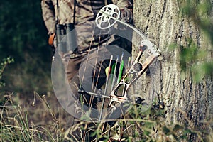 Close up shot of a hunter dressed in camouflage clothing holding a modern bow.