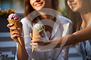Close up shot of ice cream cones in hand of a woman standing with her friend. Two young women outdoors eating icecream photo