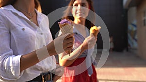 Close up shot of ice cream cones in hand of a woman walking with her friend. Two young women outdoors eating icecream on