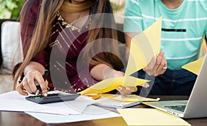 Close up shot of indian couple hands calculating budget or expenses by holding bill papers at home - concept of