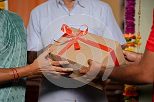 close up shot of Indian couple hands receiving parcel or gift box from delivery person at home - concept of online