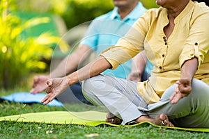 Close up shot of indian senior couple doing meditation or yoga while sitting on park - concept of wellness, healthy