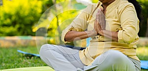 Close up shot of indian senior woman doing namaste or mudra yoga or meditation at park - concept of wellness, Active