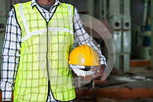 Close up shot of industrial worker standing by holding safety helmet at factory - concept of work ware, safety measures