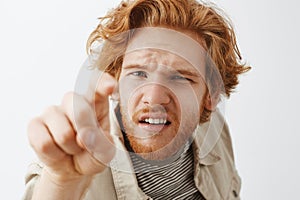 Close-up shot of intense funny and confused redhead young guy with messy hair and beard squinting poking camera with