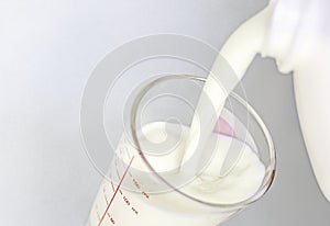Close-up shot isolated of fresh milk being pour from a plastic bottle into a clear glass measuring milliliter as a healthy food or