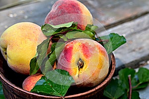 Close-up shot of juicy peaches lying in a brown ceramic plate on a wooden table