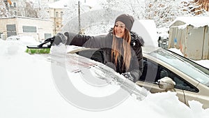 Close up shot of lady in jacket and jeans trying to clean up snow covered auto by brush. Scraping the windshield and