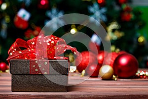 Close up shot of leather gift present box wrapped with gold dot on red ribbon bow tie placed on dark wooden table in front glossy