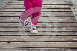 Close up shot of a little girl dressed in pink pants and shoes walking down the stairs