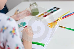 Close up shot of little girl holding brush and painting with watercolor. Selected focus