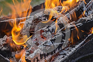 Close up shot of log pieces and fire wood, charcoal and ashes  burning in hot oranges flames in an old vintage brazier