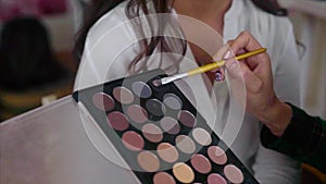 Close up shot of makeup artist taking eye shadows from make up palette by brush