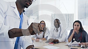 Close up shot of male doctor writting on the board during lection in the young intern in the conference room.