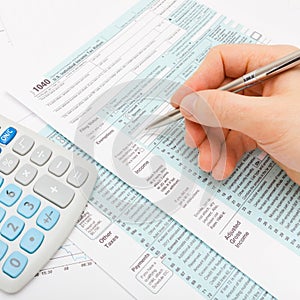 Close up shot of a male filling out US 1040 Tax Form with calculator next to it - close up studio shot