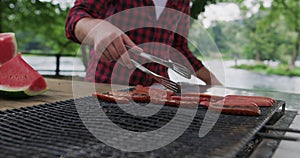 Close up shot of man cooking meat on barbecue outside in nature beside river and preparing for dinner in nature