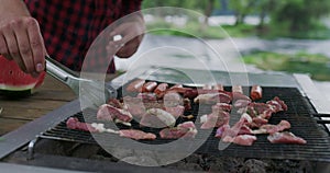 Close up shot of man cooking meat on barbecue outside in nature beside river and preparing for dinner in nature