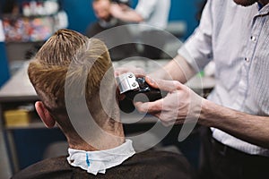 Close up shot of man getting trendy haircut at barber shop. Male hairstylist serving client, making haircut using machine and comb
