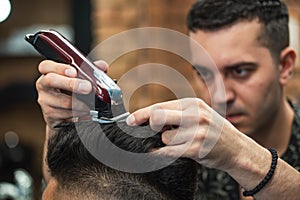 Close up shot of man getting trendy haircut at barber shop. Male hairstylist serving client, making haircut using machine and comb