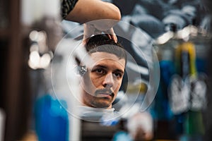 Close up shot of man getting trendy haircut at barber shop. Male hairstylist serving client, making haircut using machine and comb