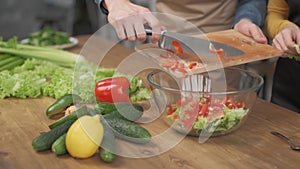 Close up shot of man hands slicing vegetables on wooden cutting board for salad on the table with healthy food in the