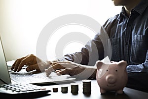 Close-up shot of man`s hand using keyboard of laptop computer with money stack step up