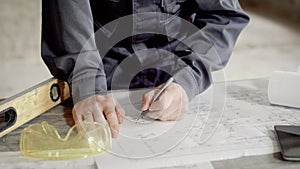 Close up shot of at the man`s hands, who makes notes in the construction drawing for the foreman and builders, the man