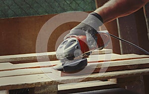 Close-up shot of a man sanding a wood board with an angle grinder at workshop, woodworking scene