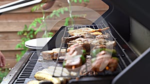 Close up shot of man using tongs to barbeque meat and sausages or bratwurst on a grill in backyard