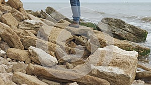 A close-up shot of a man wearing a pair of jeans and brown boots walking on a rocky coastline.