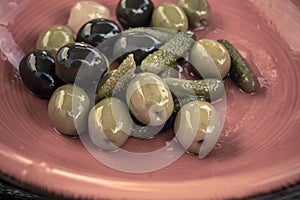 Close-up shot of mix of black and green olives with pickle in an orange bowl