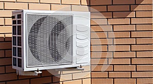 Close-up shot of a modern climate control unit against the background of a brick wall of the facade of a house outside. Air