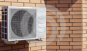 Close-up shot of a modern climate control unit against the background of a brick wall of the facade of a house outside. Air