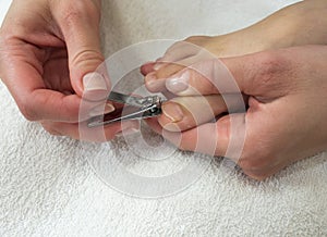 Close-up shot of a mother gently holding her little child& x27;s foot and cutting toenails on white towel.