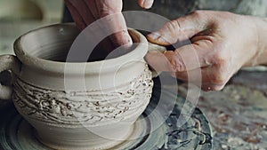 Close-up shot of muddy male potter`s hands shaping and fixing ears of ceramic bowl. Nimble craftsman is forming clay