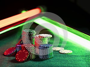Close-up shot of a multicolored chips piles, some of them laying nearby on green cover of playing table, under green and