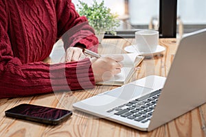 Close-up shot of online studying woman writing notes while sitting in front of her computer laptop at living room.