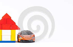 Close up shot of an orange sport car and a house toy with copy space on white background
