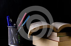 Close up shot of a pen stand with stationary items in it and pile of books with one opened -Higher Study concept