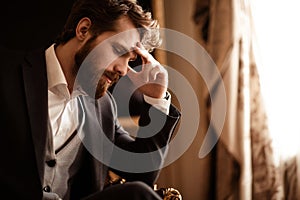 Close up shot of pensive bearded man in elegant formal suit, ponders about something, has some problems with finances