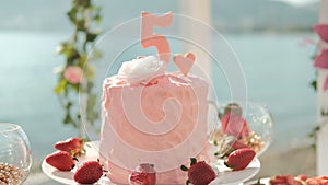 Close-up shot of pink big birthday cake with cream number five on festive table