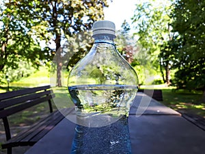 Close up shot of plastic bottle with white cap filled with water on the brown outdoor camping table with green nature background