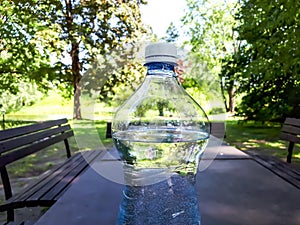 Close up shot of plastic bottle with white cap filled with water on the brown outdoor camping table with green nature background