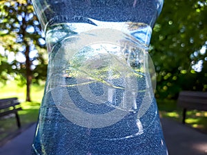 Close up shot of plastic bottle with white cap filled with water on the brown outdoor camping table with green nature background