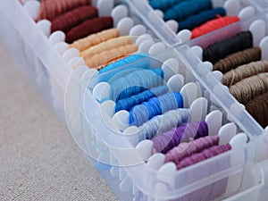 A close-up shot of a plastic sorting box full of bobbins with different colour embroidery threads on a beige canvas background