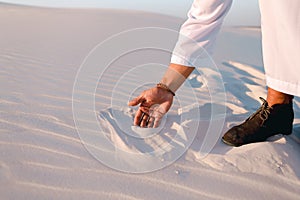 Close-up shot of portrait and hands of young Arab guy in sandy desert on clear summer day in open air.