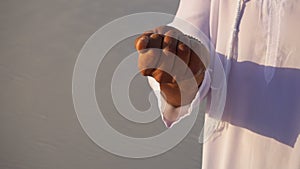 Close-up shot of portrait and hands of young Arabian Sheikh guy in sandy desert on clear summer day in open air.