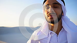 Close-up shot of portrait of happy sheik boy standing in middle of sandy desert and enjoying scenery on warm summer